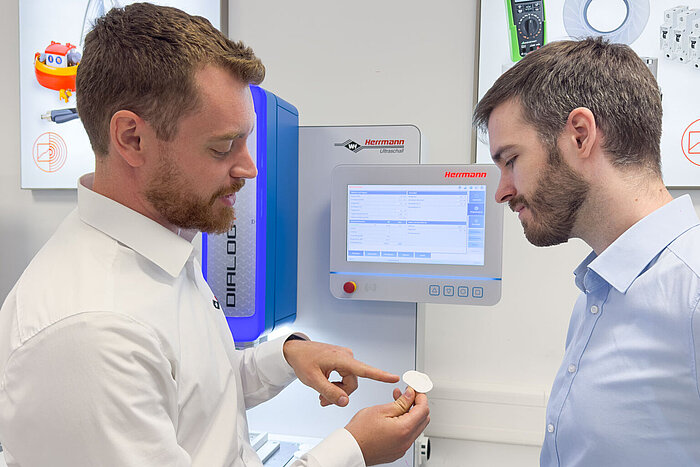 Two people inspect an ultrasonic weld between film and plastic in a laboratory