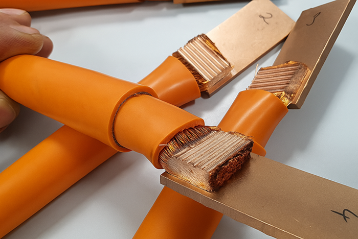 Orange isolierte Kupferkabel mit freigelegten Litzenenden, die an flache Kupferschienen angeschlossen sind.