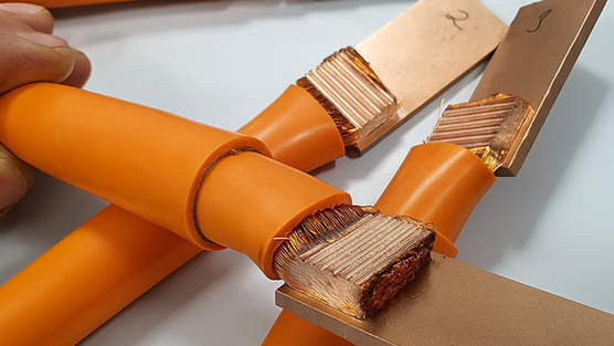 Orange isolierte Kupferkabel mit freigelegten Litzenenden, die an flache Kupferschienen angeschlossen sind.